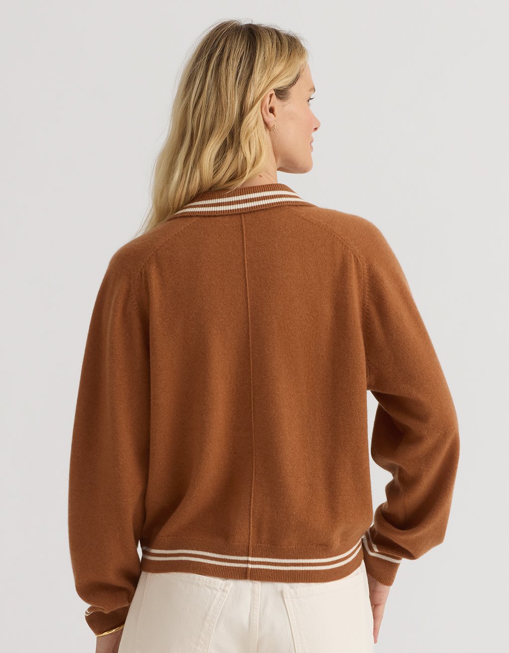 Back view of a woman wearing a burnt orange cashmere polo sweater on a plain background