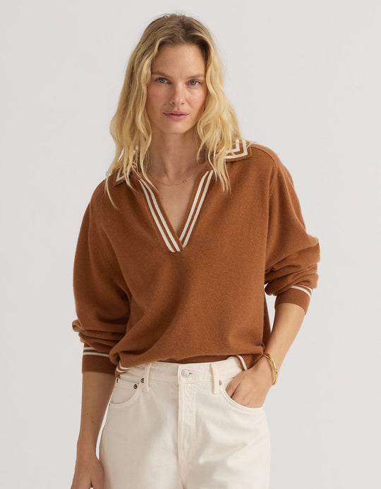 Woman wearing a burnt orange cashmere polo sweater with white trim and cream jeans on a plain background