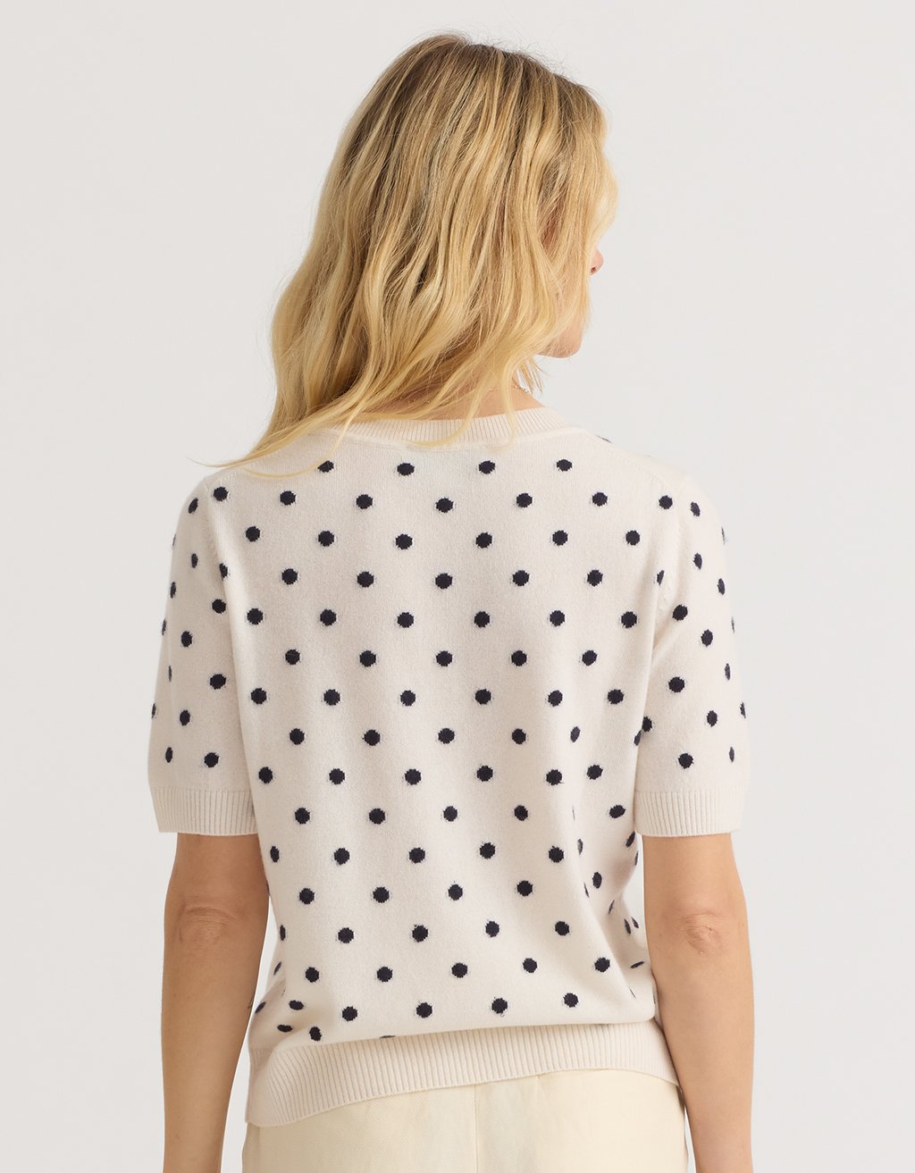 Back view of a woman wearing a polka dot cashmere tee on a plain background
