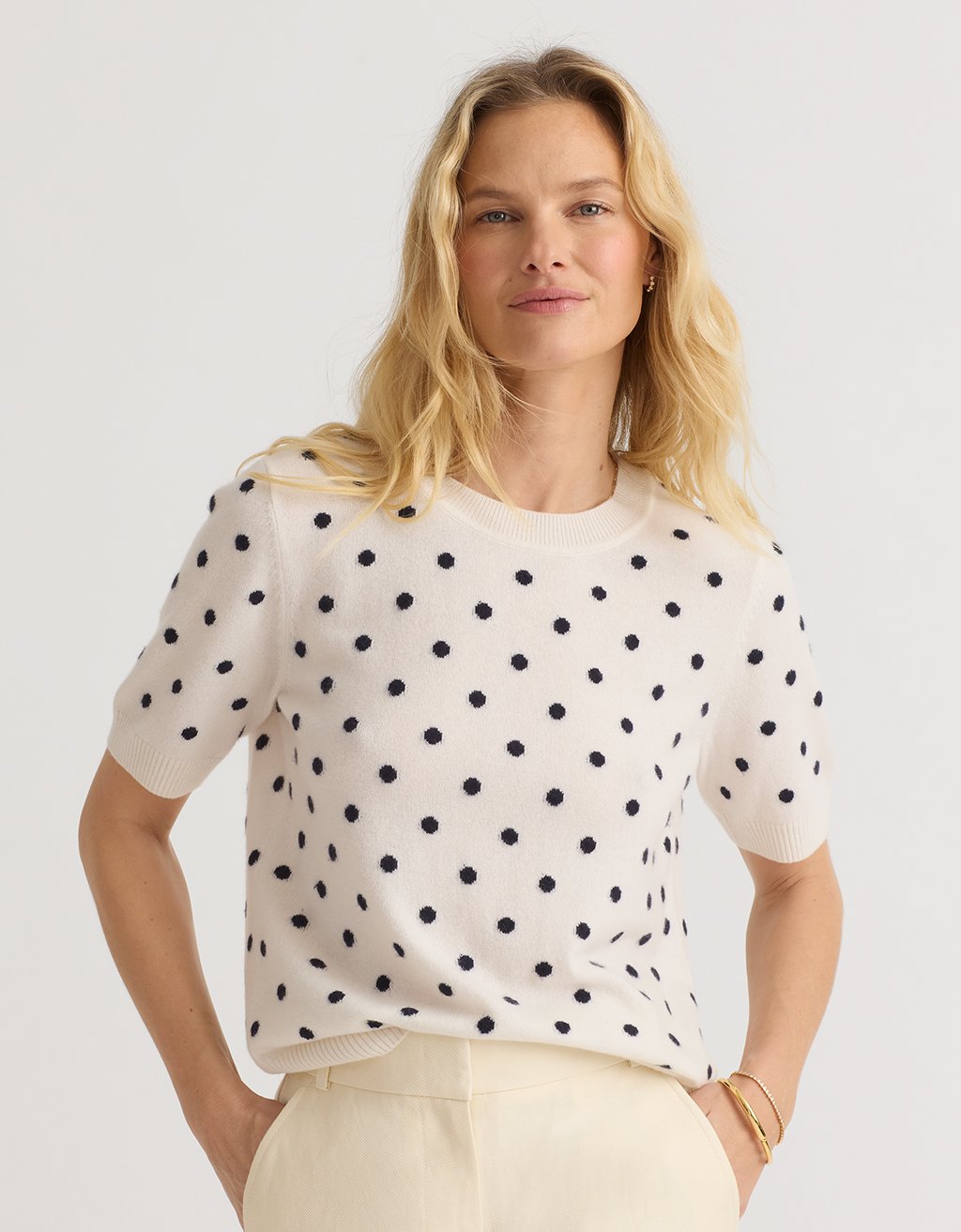 Woman wearing a cream cashmere tee with polka dots on a plain background
