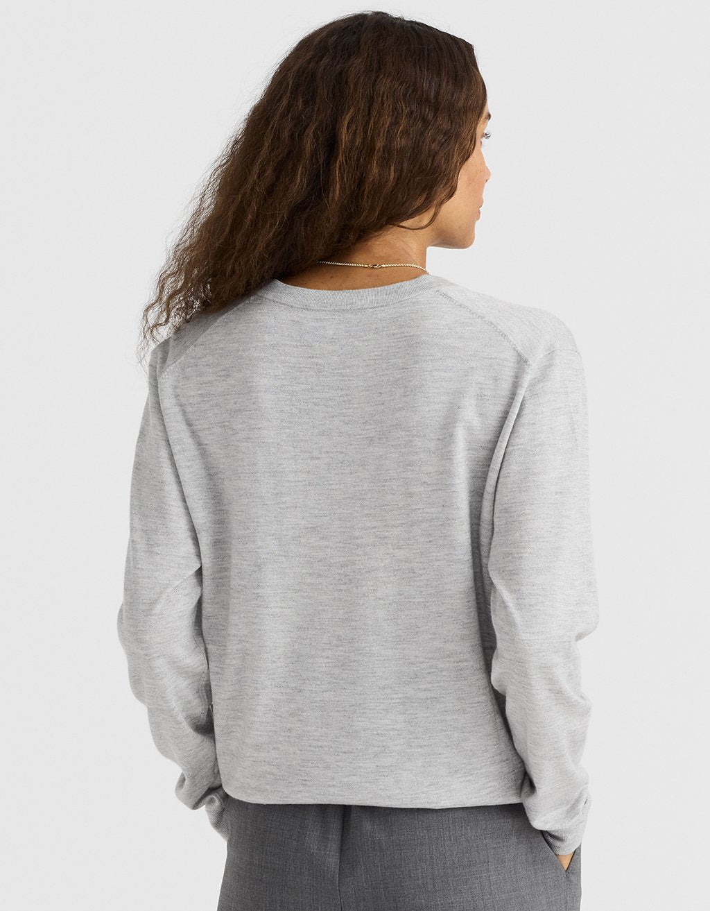 Back view of a woman wearing a light gray cashmere sweater on a light gray background