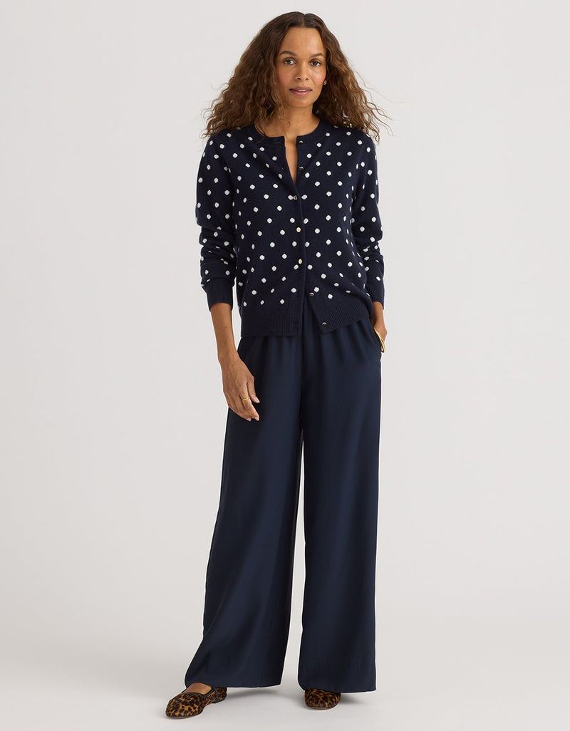 Woman wearing a navy polka dot cashmere cardigan and navy wide-leg pants on a light gray background