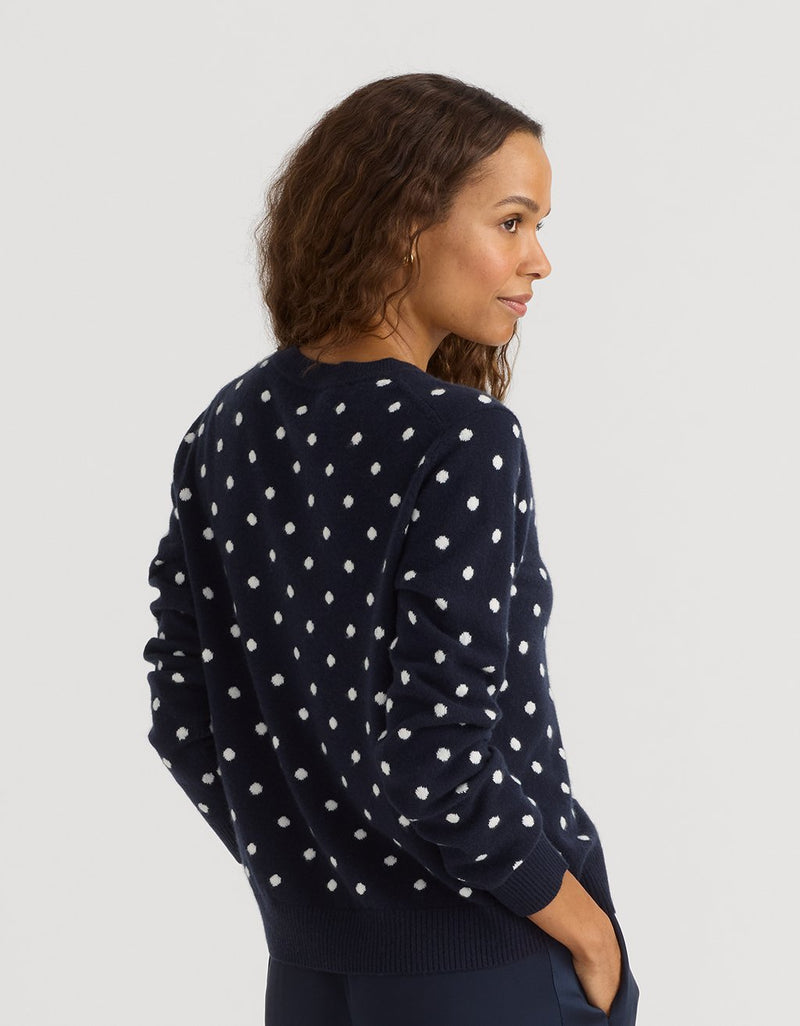 Woman wearing a navy blue sweater with white polka dots on a light gray background