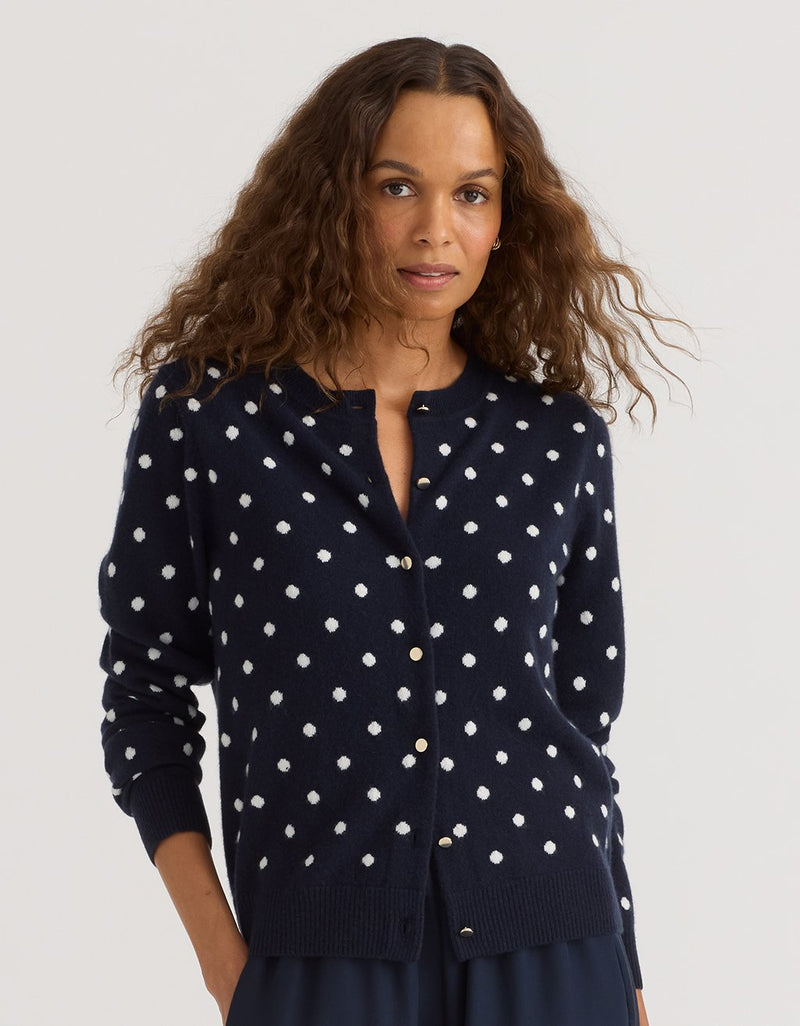 Woman wearing a navy blue cashmere cardigan with white polka dots on a plain background