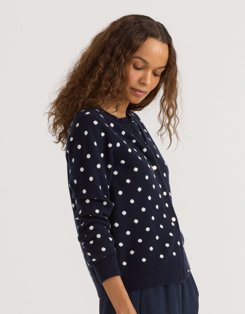 Woman wearing a navy blue sweater with white polka dots on a plain background