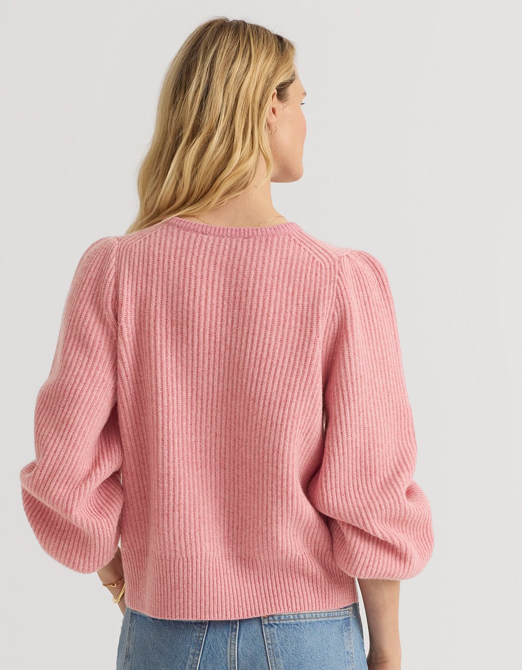Back view of a woman wearing a pink cashmere puff sleeve cardigan on a light gray background