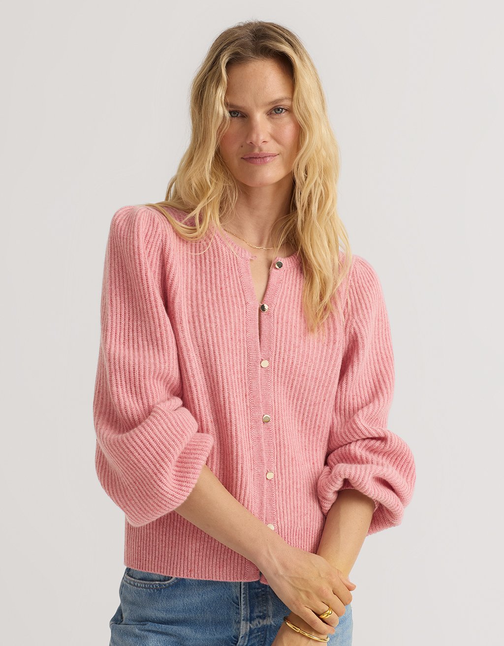 Woman wearing a pink cashmere puff sleeve cardigan with a plain background