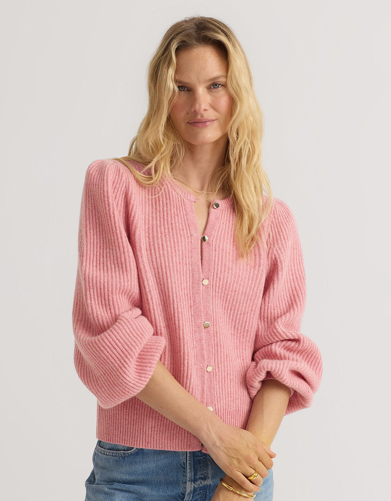 Woman wearing a pink cashmere puff sleeve cardigan with a plain background
