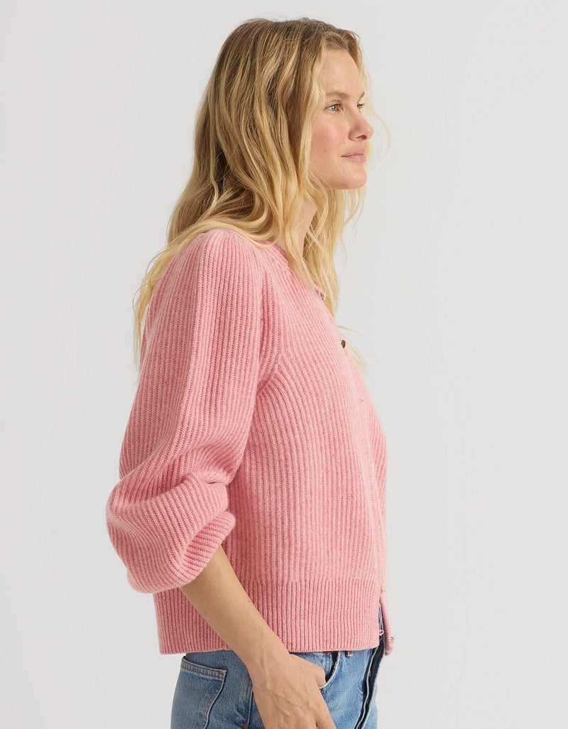 Woman wearing a pink cashmere puff sleeve cardigan on a light gray background