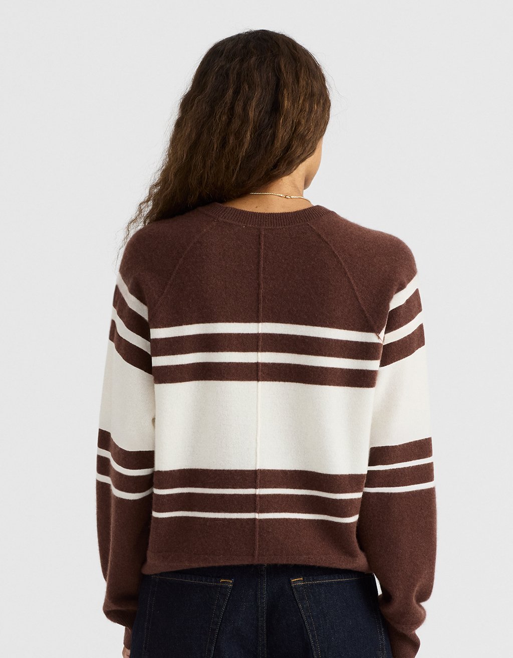 Back view of a woman wearing a brown and white striped cashmere sweater on a light gray background
