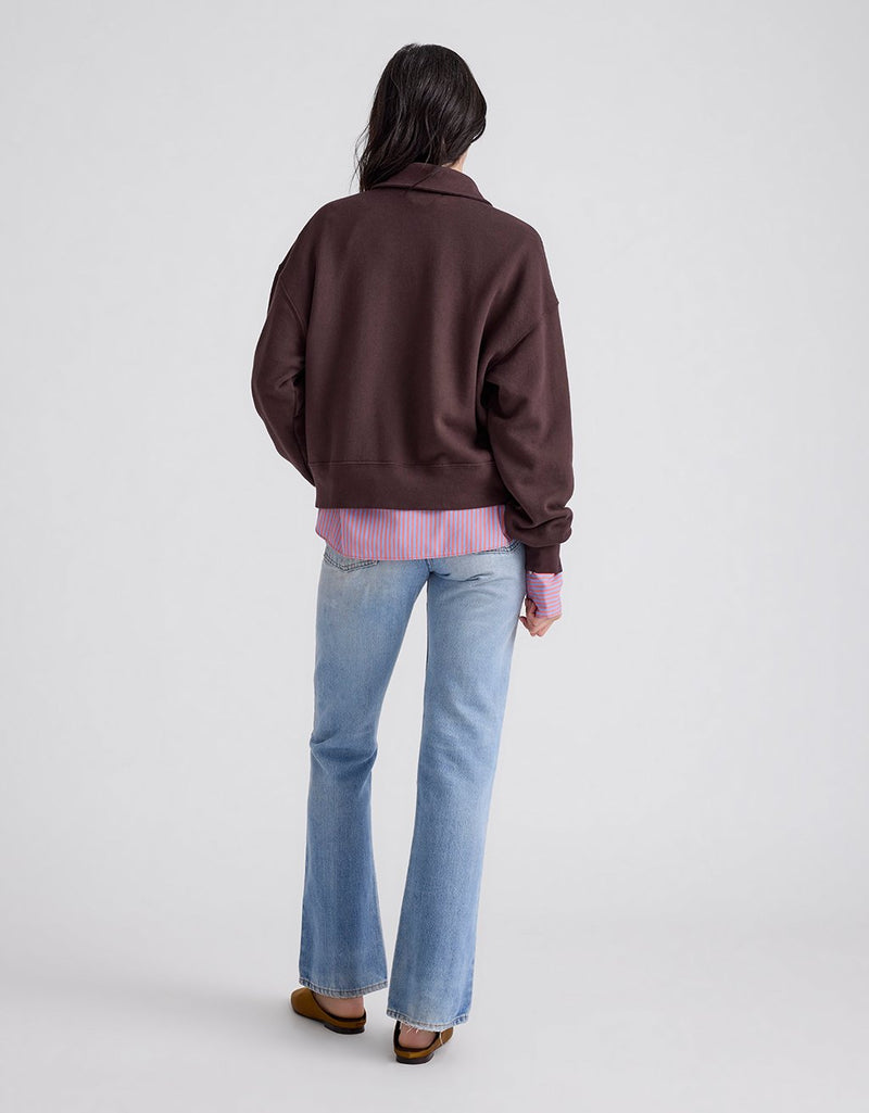 Back view of a person wearing a dark brown polo sweatshirt on a light gray background