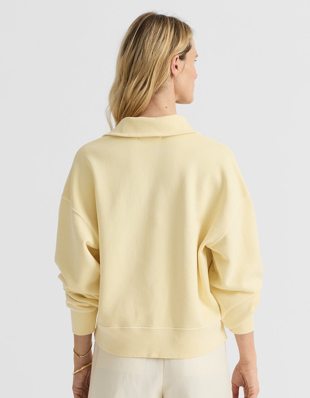Woman wearing a light yellow polo sweatshirt against a white background