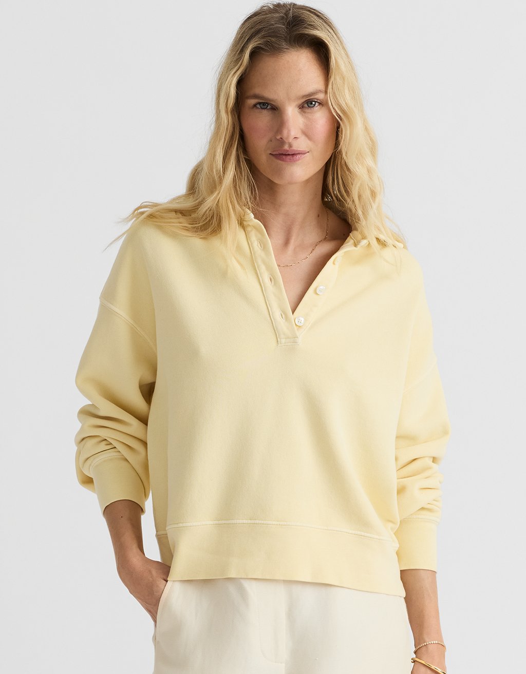 Woman wearing a light yellow polo sweatshirt against a plain background