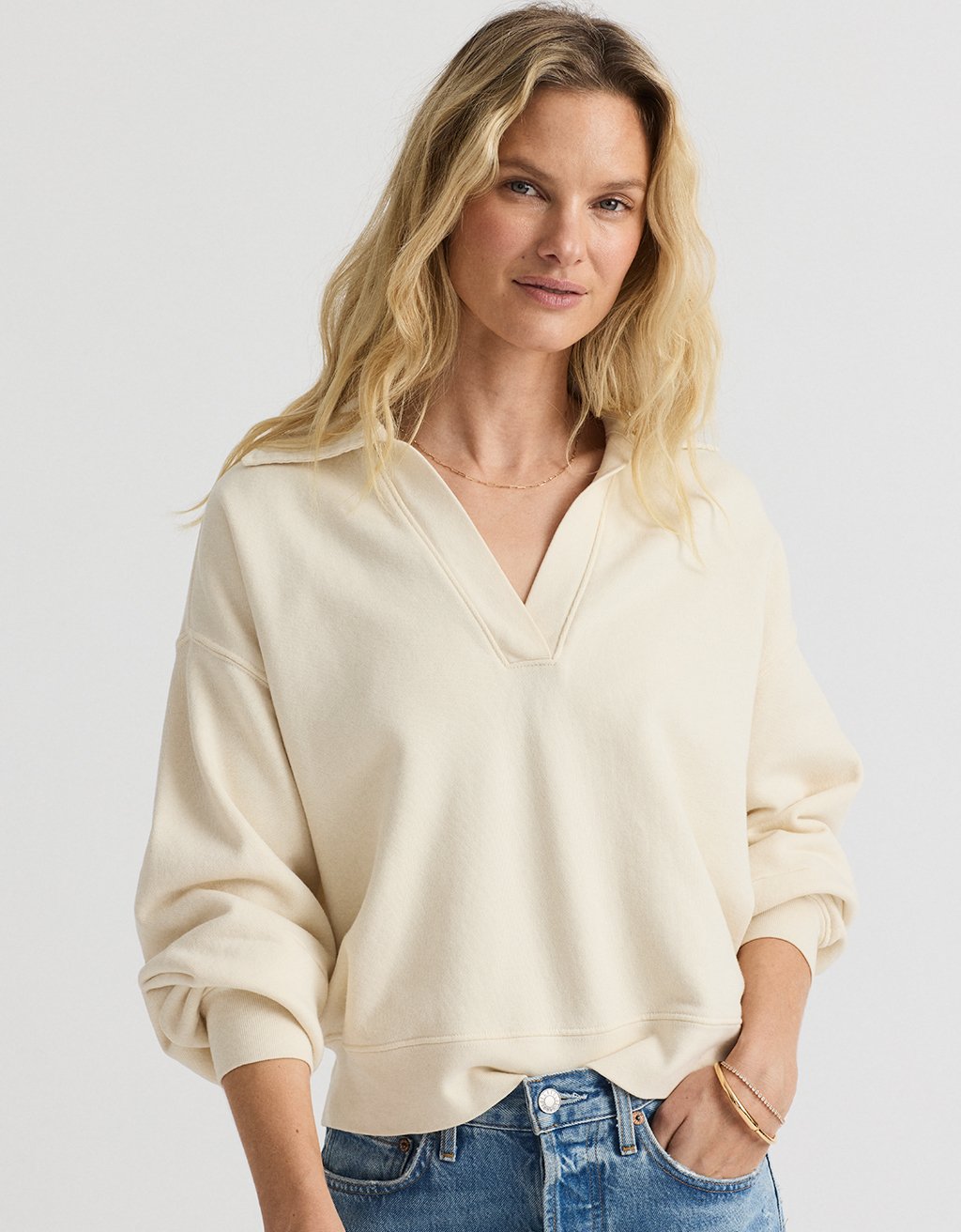 Woman wearing a cream colored sweatshirt and blue jeans on a white background