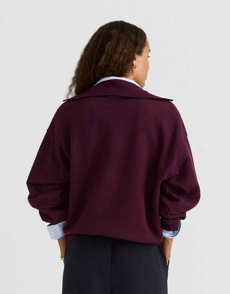 Woman wearing a burgundy polo sweatshirt on a plain background