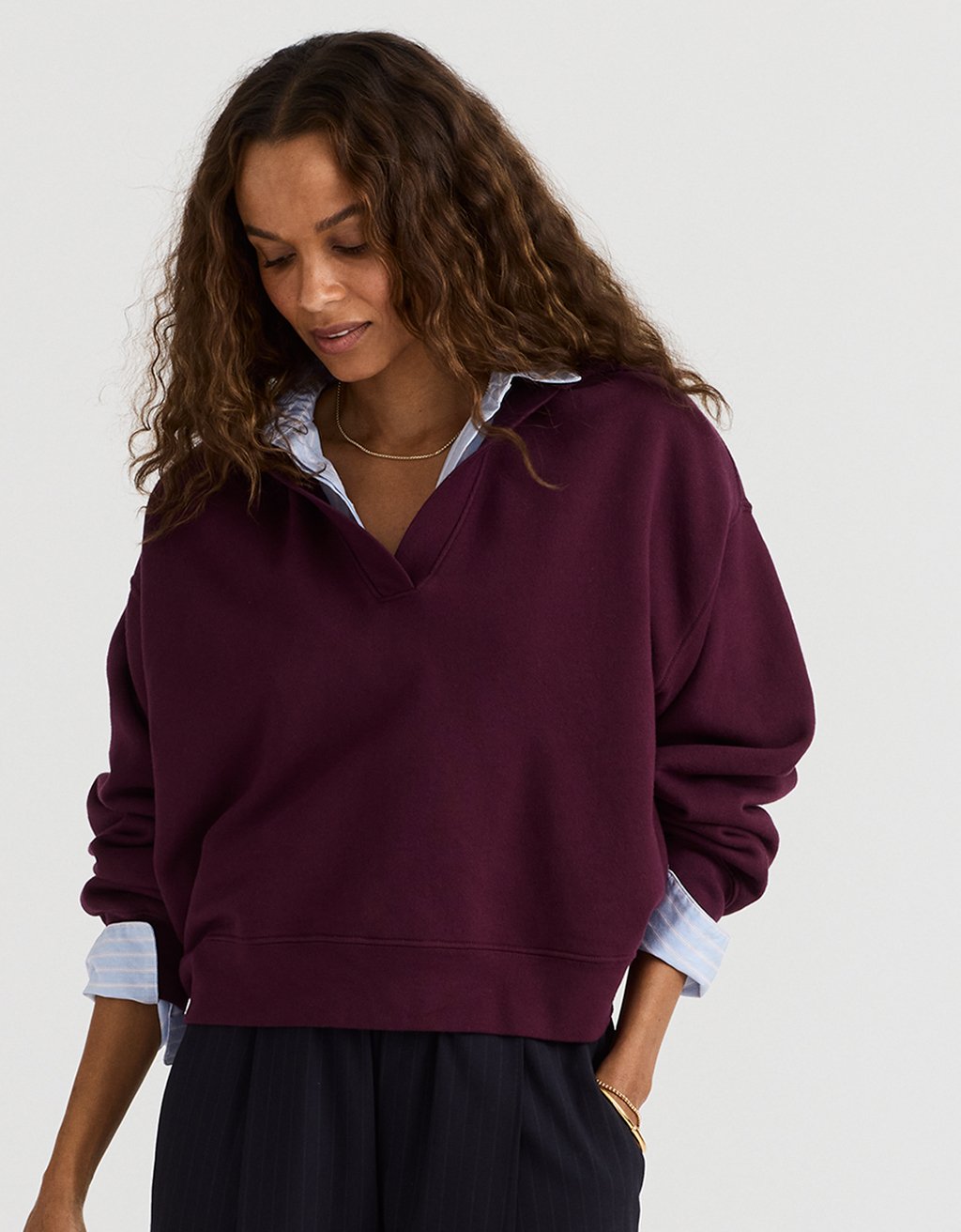 Woman wearing a burgundy sweater over a button down shirt with a neutral background