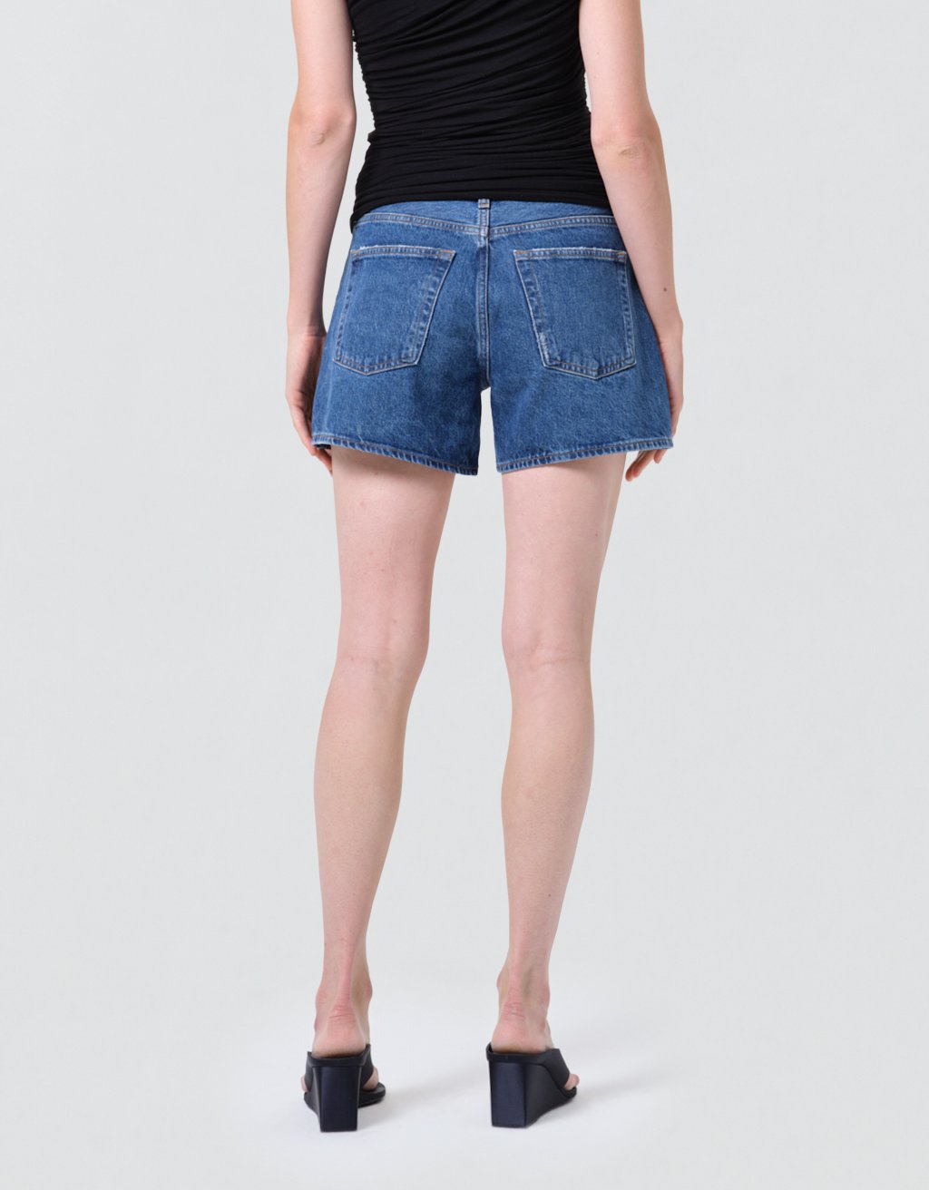 Back view of a person wearing high-rise blue denim shorts on a plain background