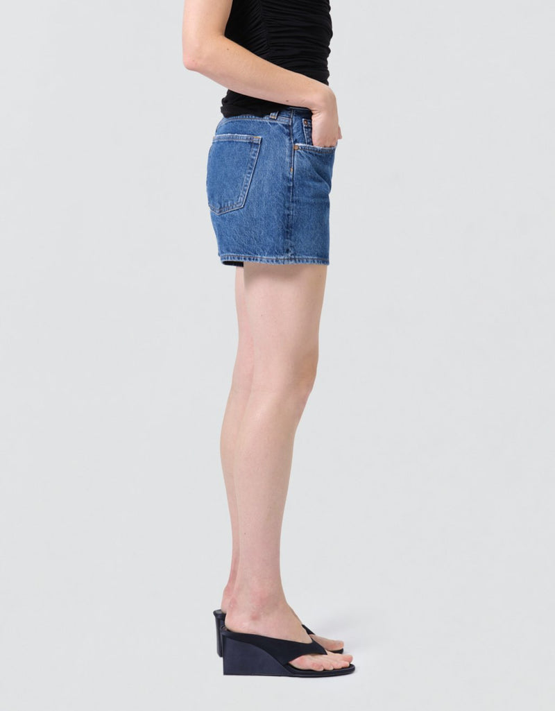 Side view of a person wearing high-rise blue denim shorts on a plain background