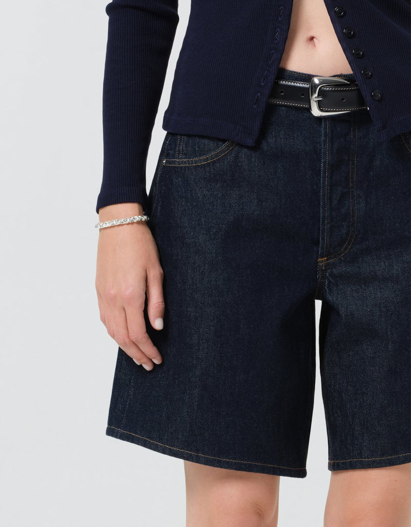 Close-up of a person wearing dark blue denim shorts with a plain background