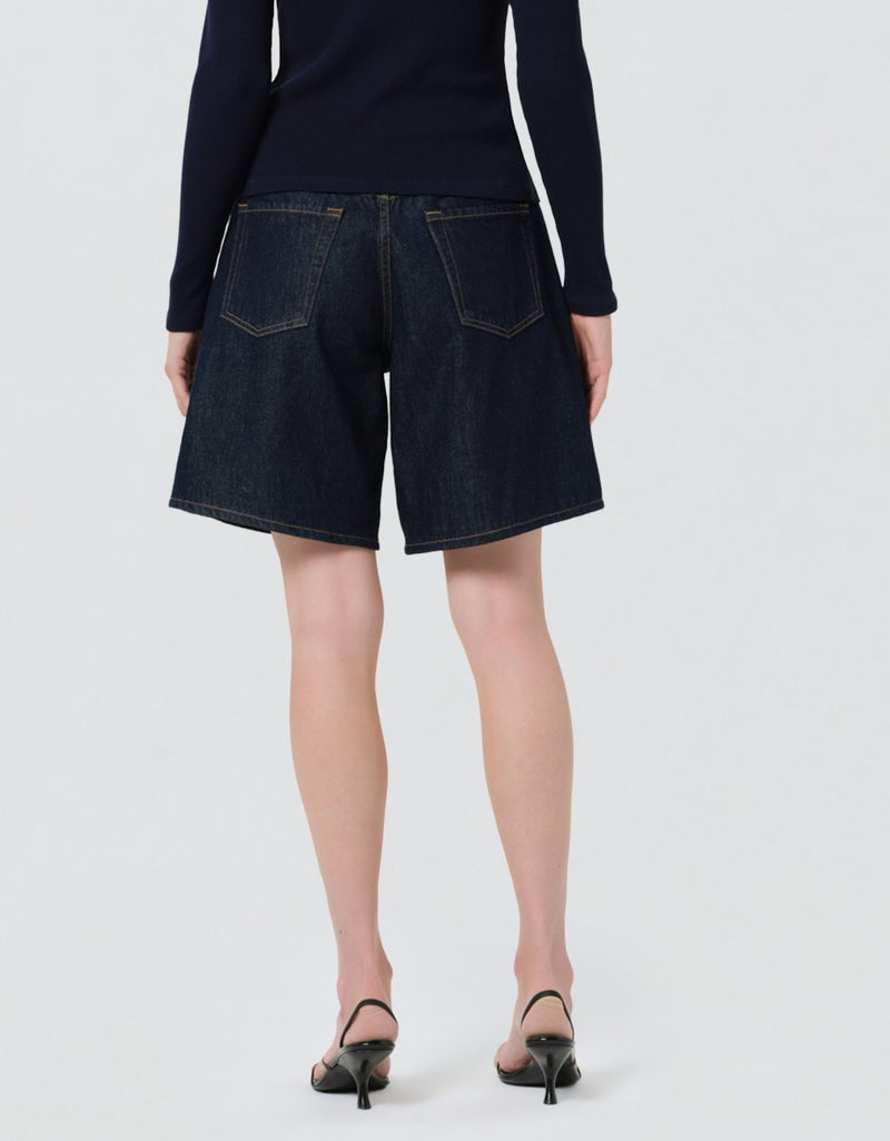 Back view of a person wearing dark denim shorts and a navy cardigan on a light gray background