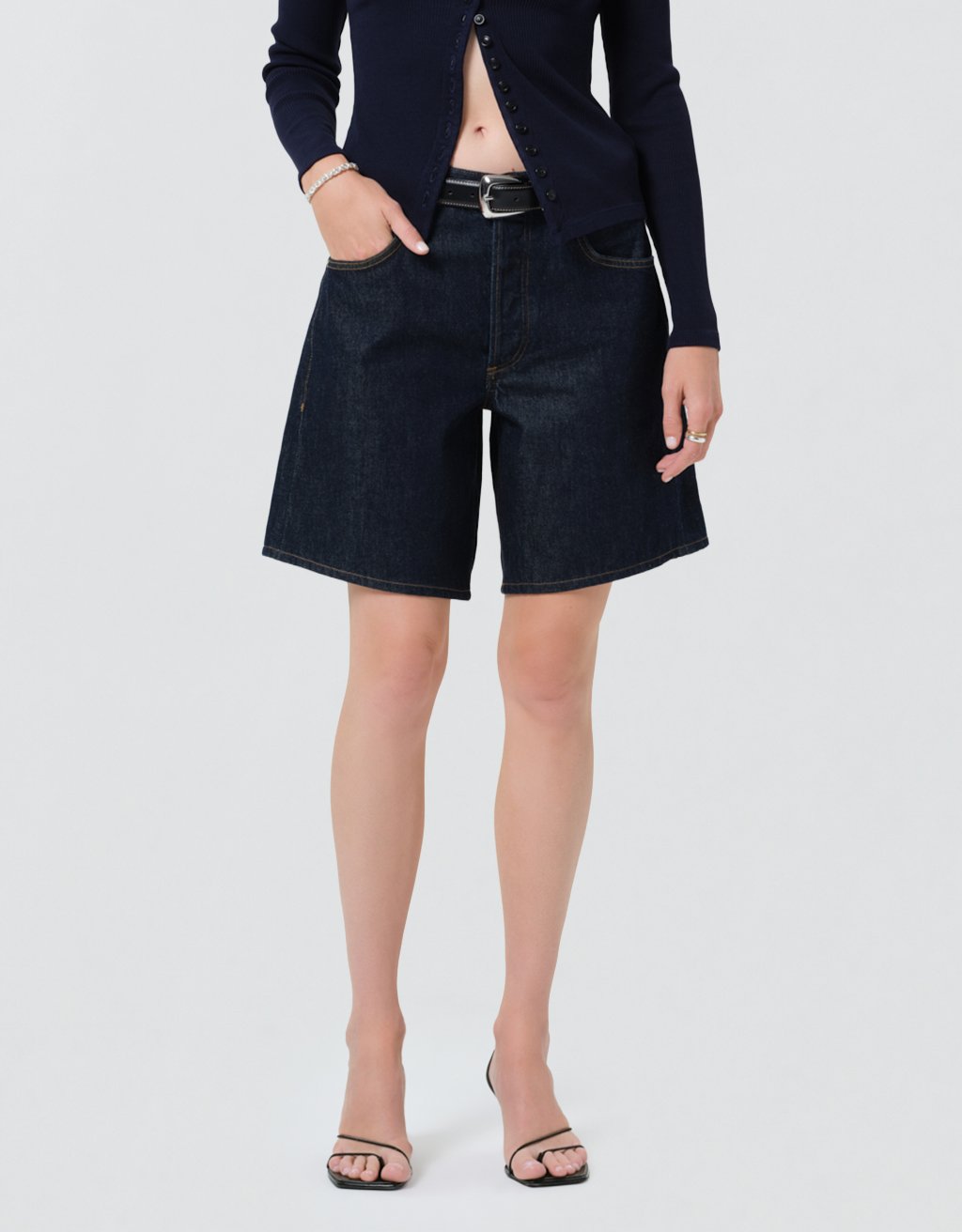 Person wearing dark denim shorts and a navy cardigan on a light gray background