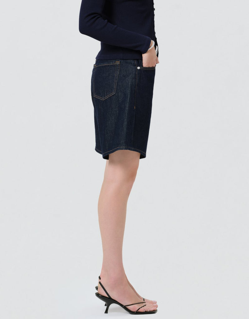 Side view of a person wearing dark denim shorts and a navy cardigan on a light gray background