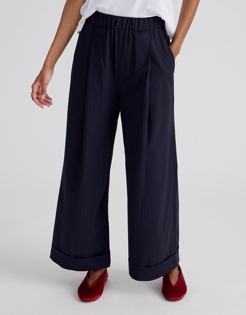 Navy pinstripe wide-leg pants worn by a person on a light gray background