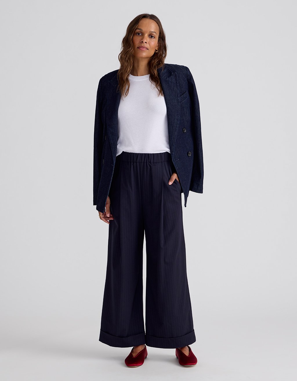 Woman wearing a green top and navy wide-leg pinstripe pants on a light gray background