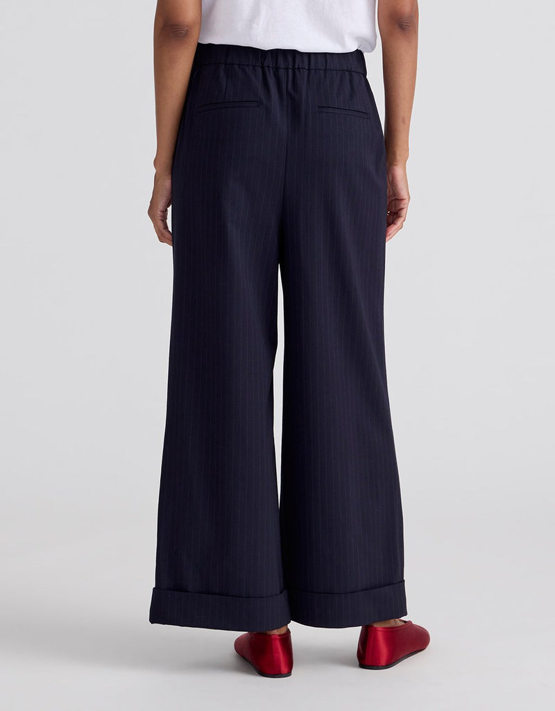 Back view of a person wearing navy pinstripe wide-leg pants and a green top on a light gray background