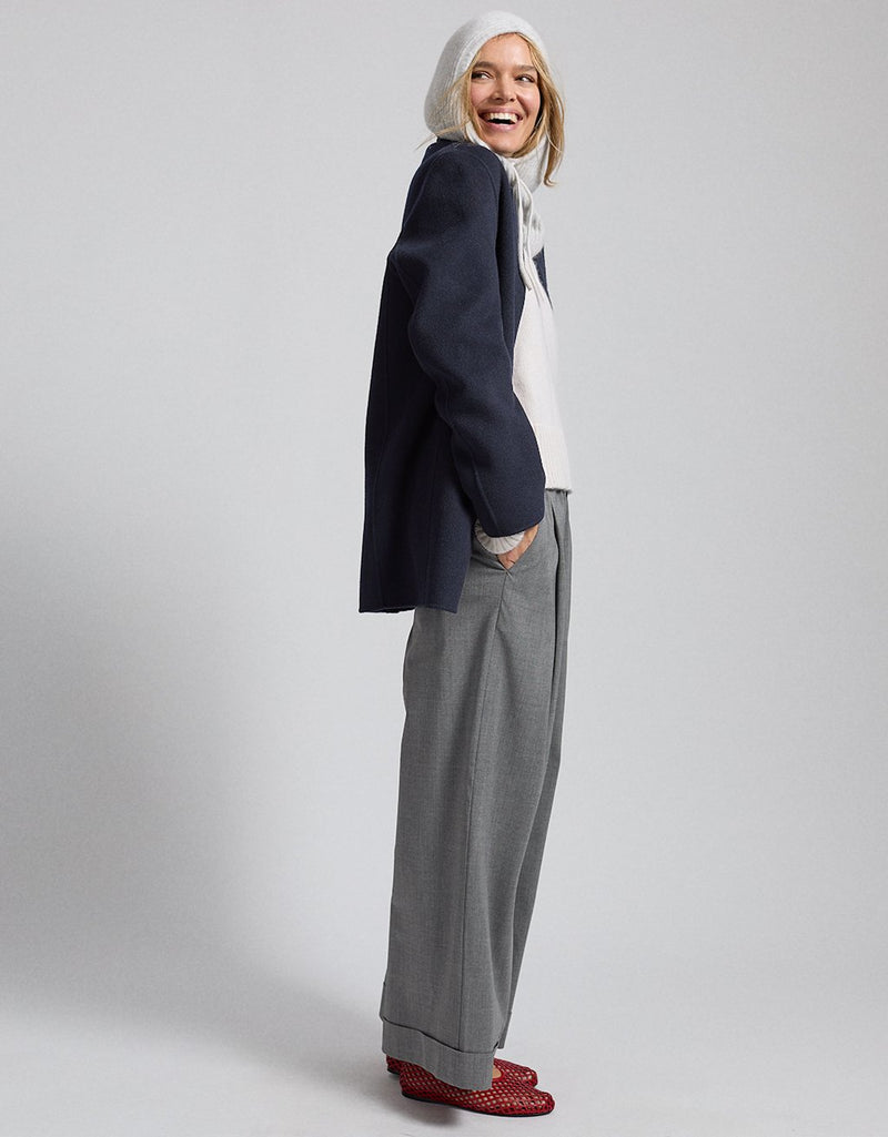 Profile of a woman wearing a navy blazer, hooded sweatshirt, gray pants, and red shoes on a light gray background