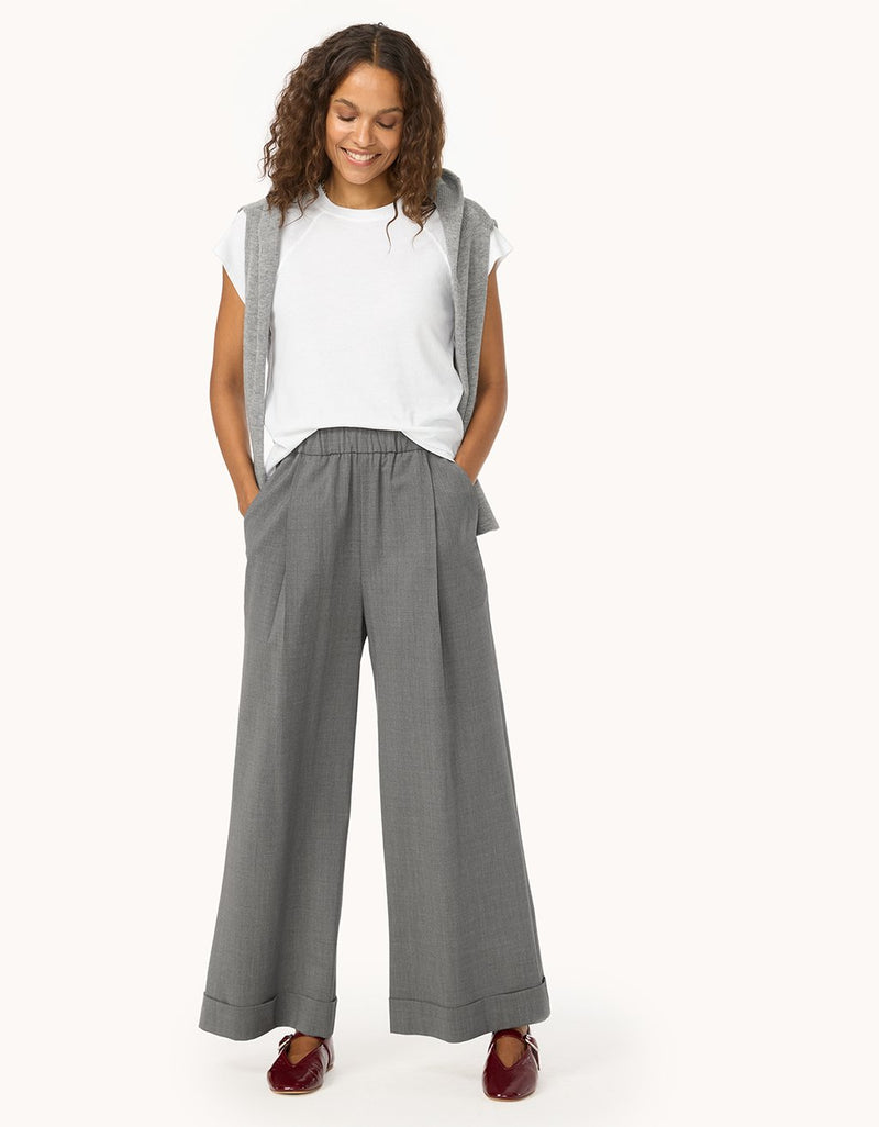 Woman wearing a white t-shirt with a gray sweater over her shoulders and wide-leg gray pants on a light gray background