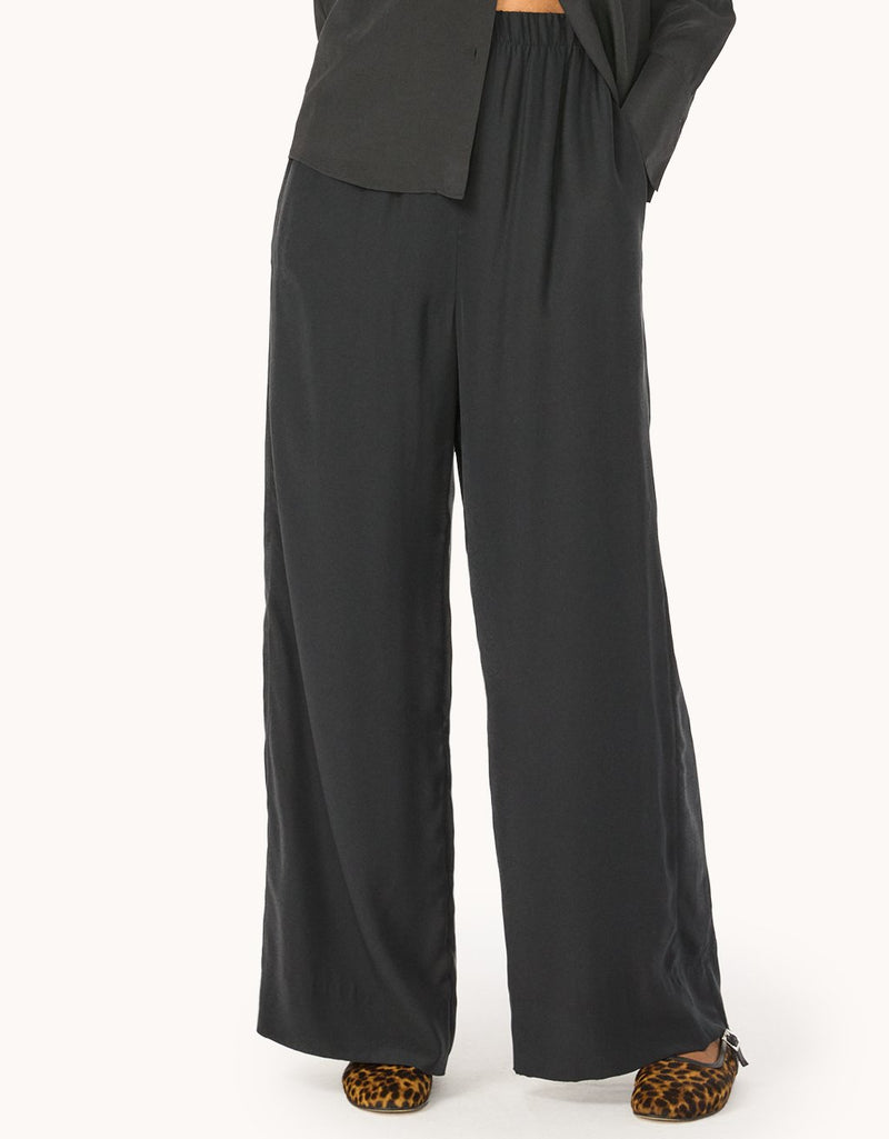 Close-up of black silk wide-leg pants worn by a person on a light gray background