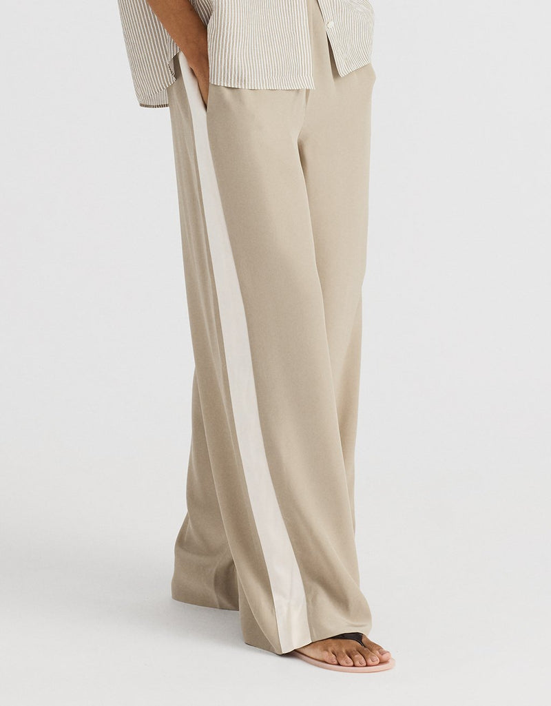 Beige silk wide leg pants with a contrast side white stripe on a light gray background