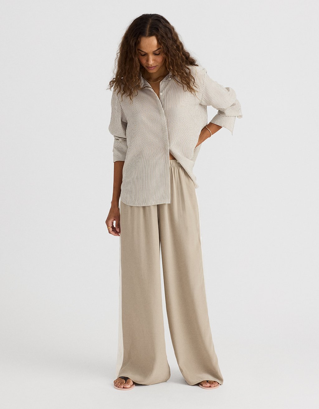 Woman wearing a striped shirt and beige silk wide leg pants on a white background