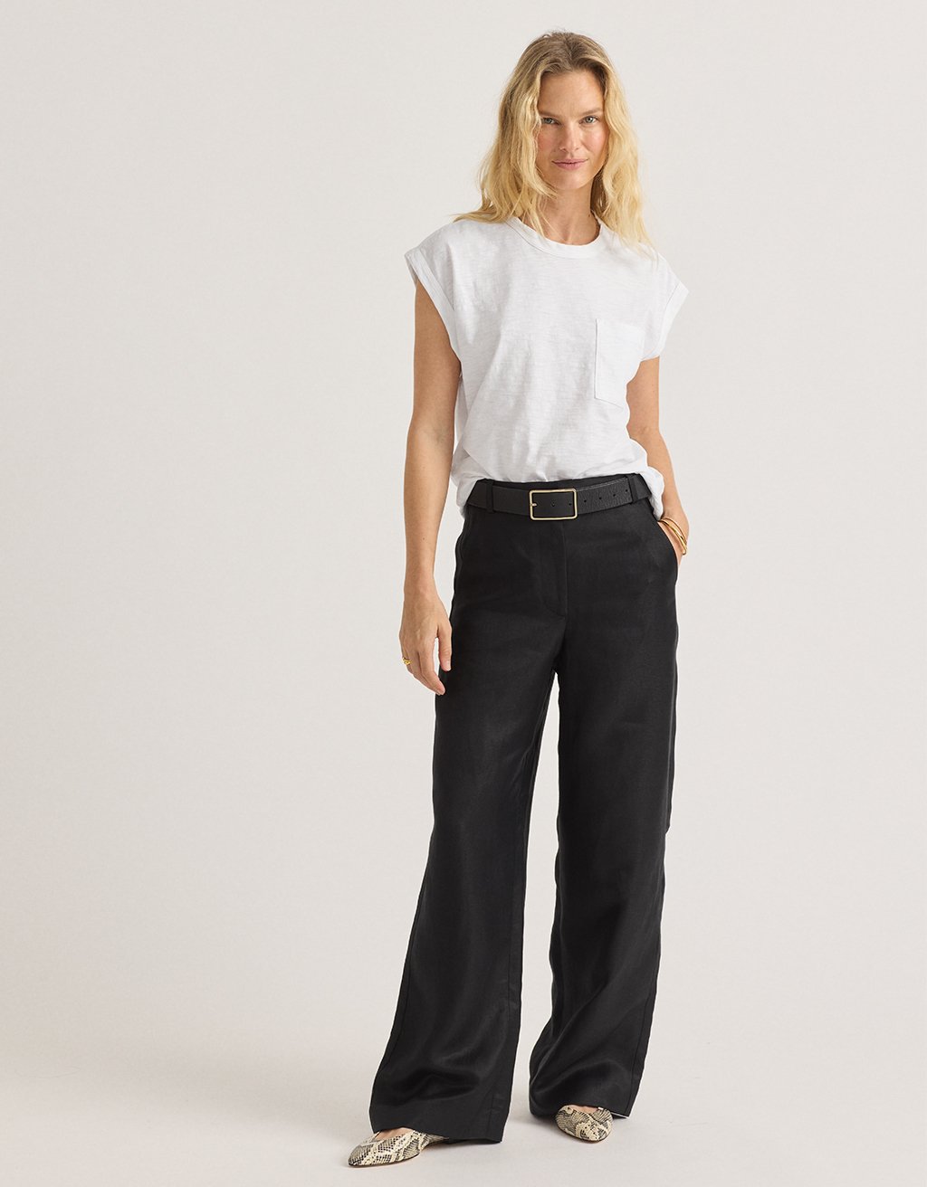 Woman wearing a white t-shirt and black wide-leg pants on a plain background