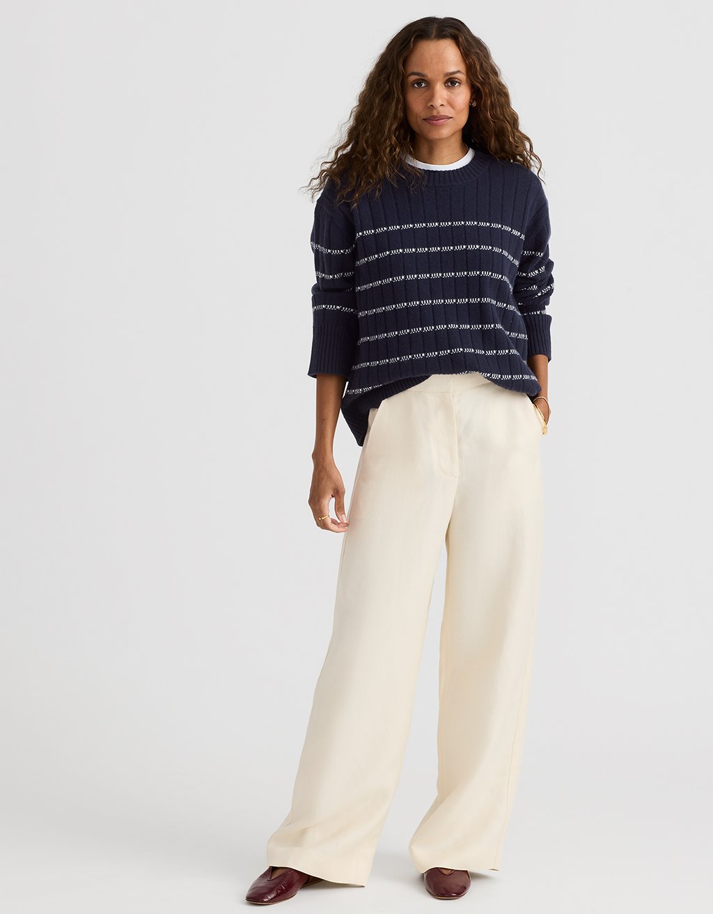 Woman wearing a navy striped sweater and cream wide leg pants on a light gray background