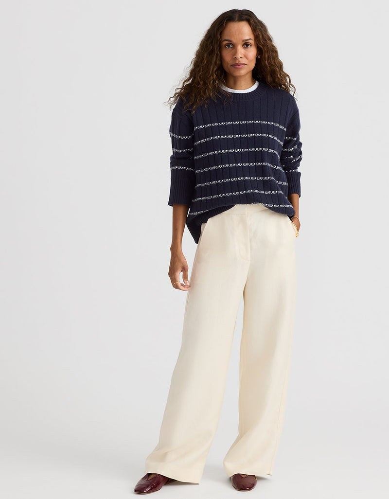 Woman wearing a navy striped sweater and cream wide leg pants on a light gray background