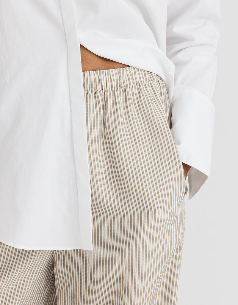Close-up of a person wearing a white shirt and beige striped pants on a light background