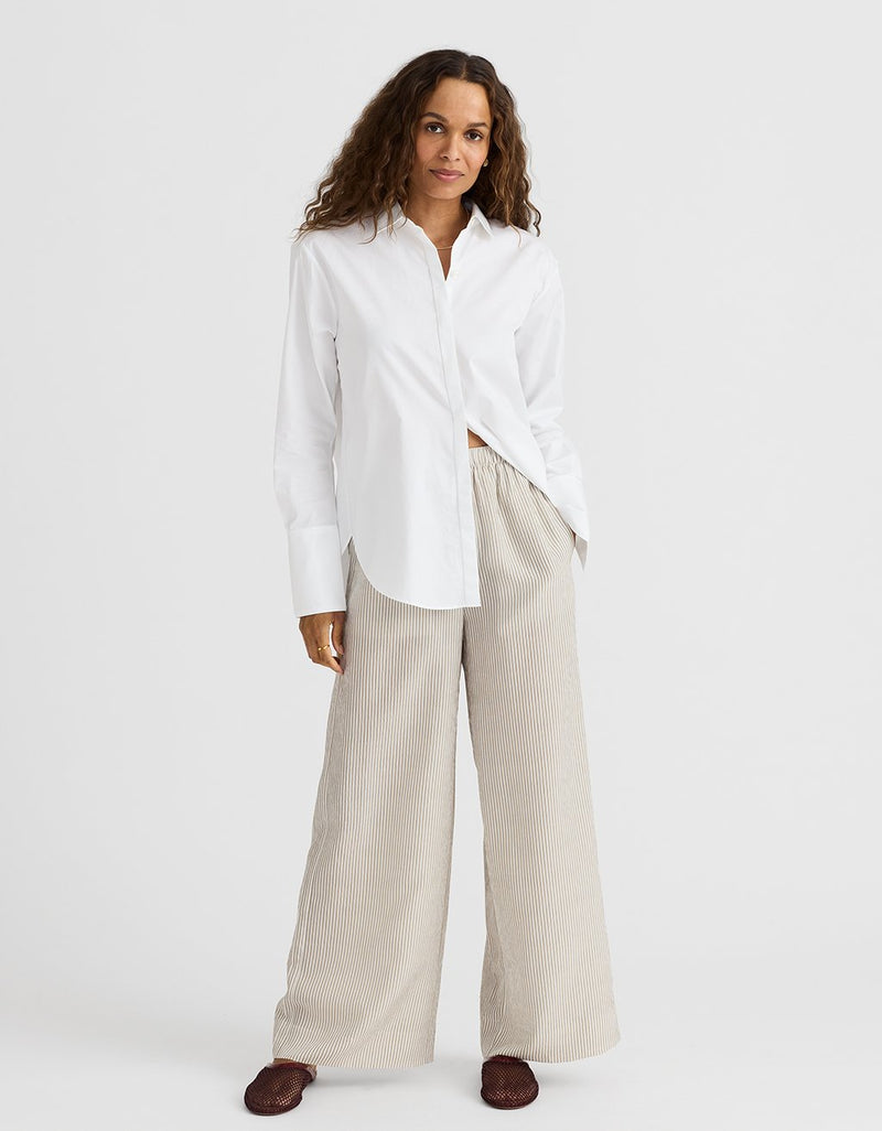 Woman wearing a white shirt and beige stripe pants on a white background