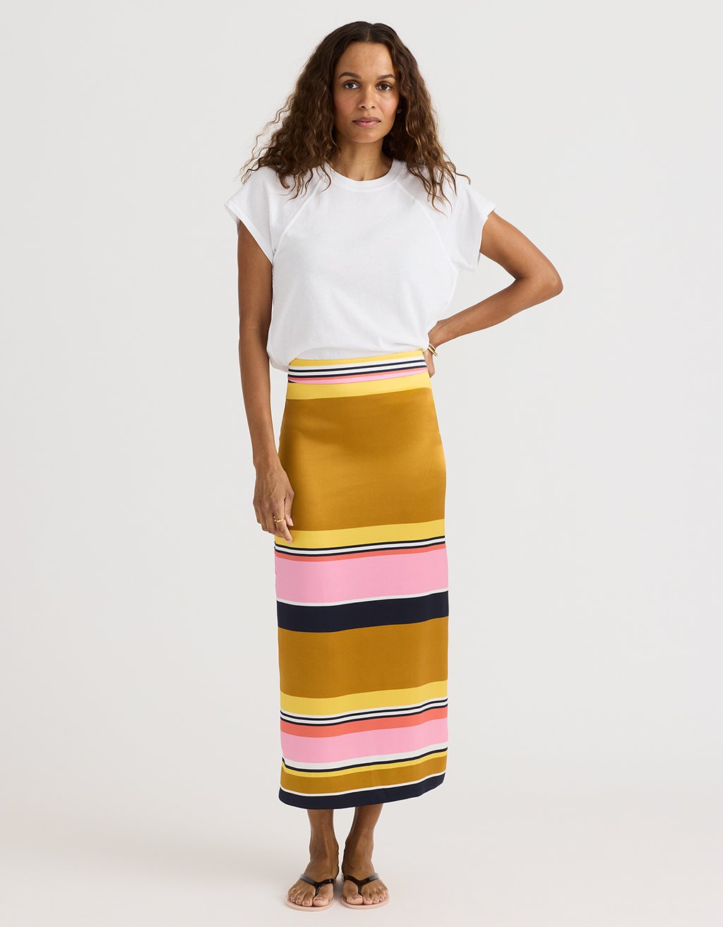Woman wearing a white top and a long, multicolored striped skirt on a white background