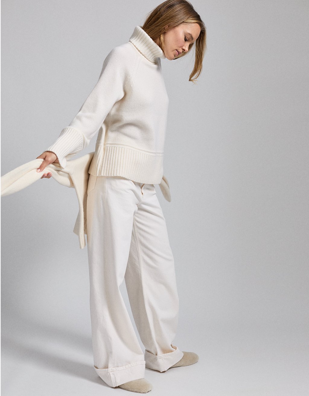 Woman wearing a cream-colored turtleneck and jeans against a plain background
