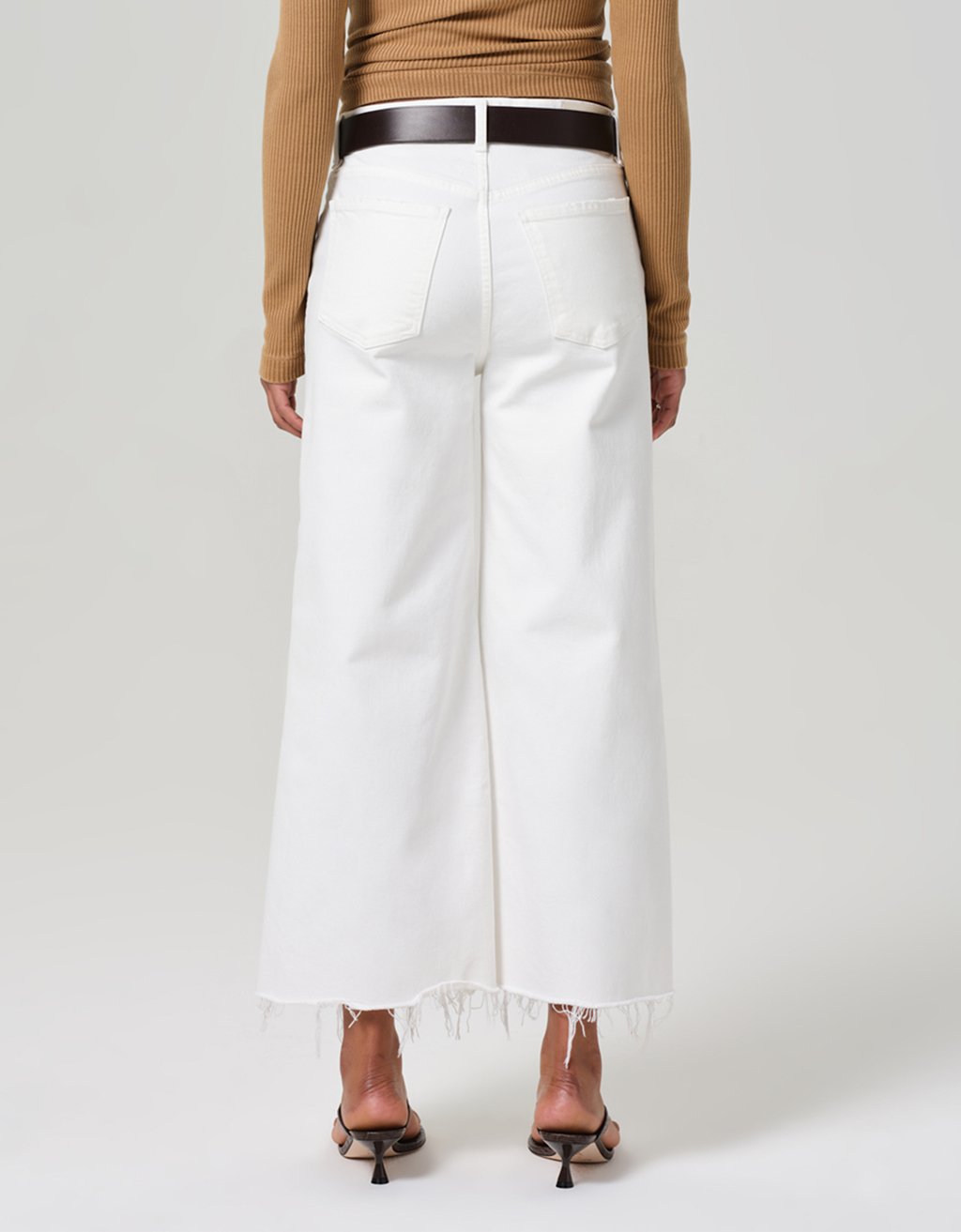 Back view of a person wearing white jeans with a brown top on a plain background
