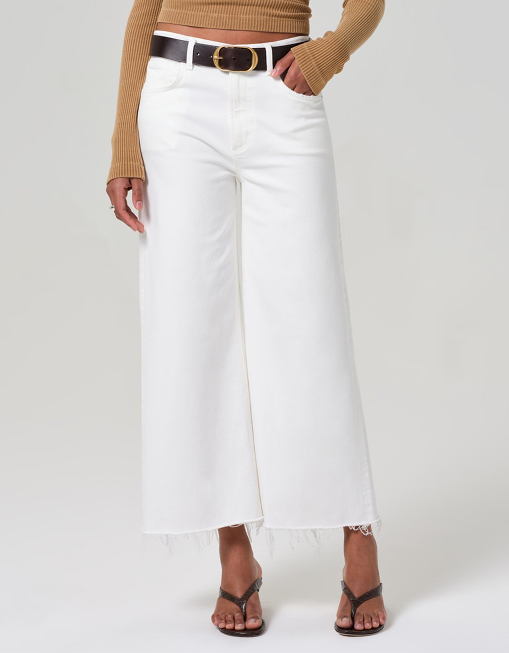 Person wearing white wide-leg jeans with a belt on a plain background