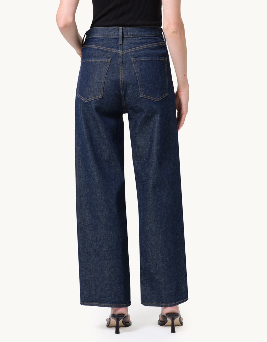 Back view of a person wearing high-rise dark blue wide-leg jeans on a light gray background
