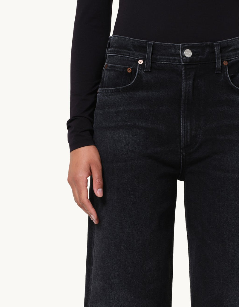 Close-up of a person wearing a black top with black jeans on a neutral background