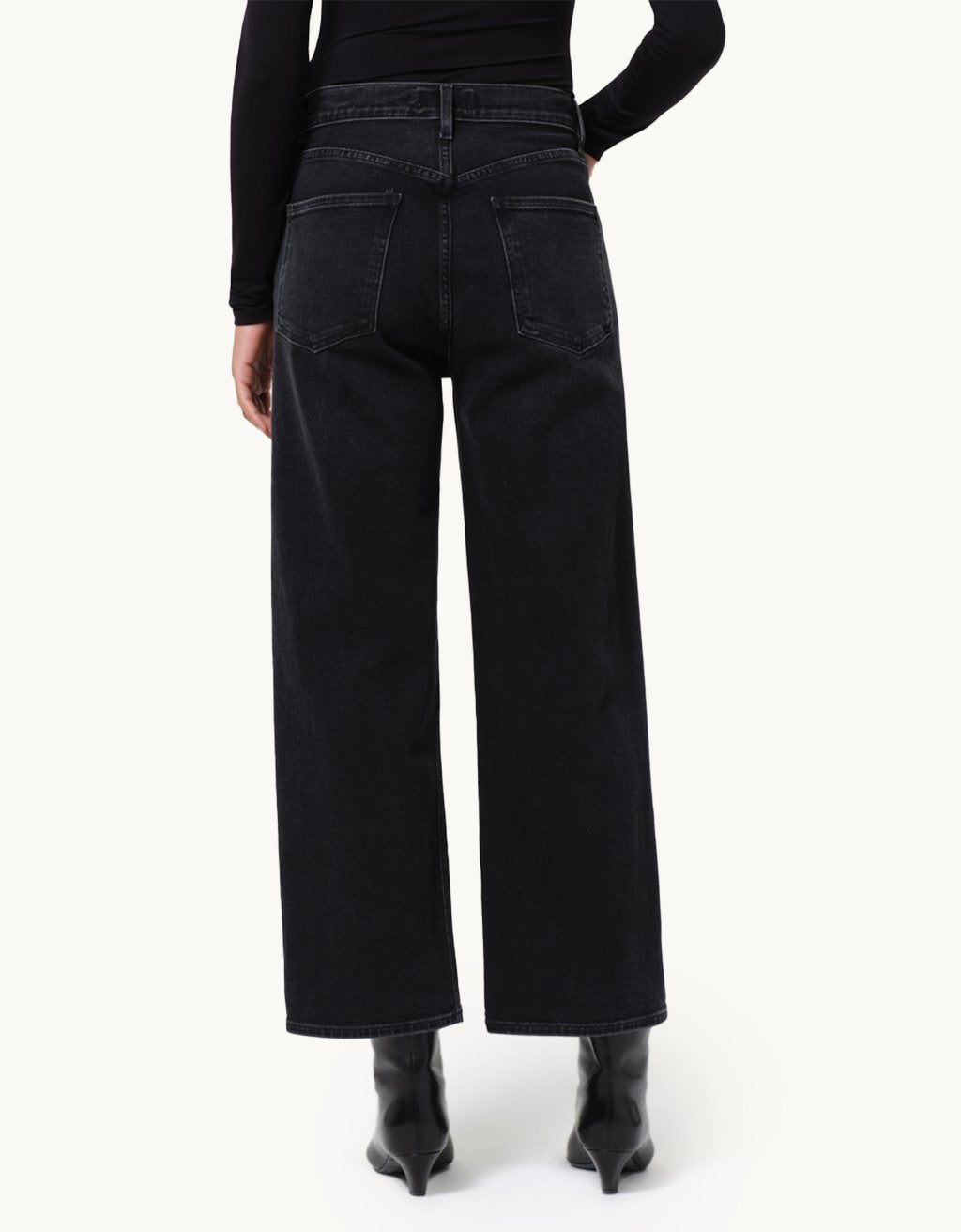 Person wearing black wide-leg jeans and a black top and booties on a neutral background
