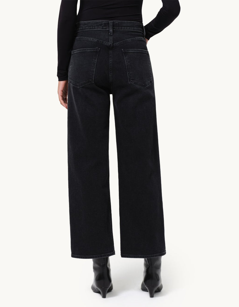 Person wearing black wide-leg jeans and a black top and booties on a neutral background