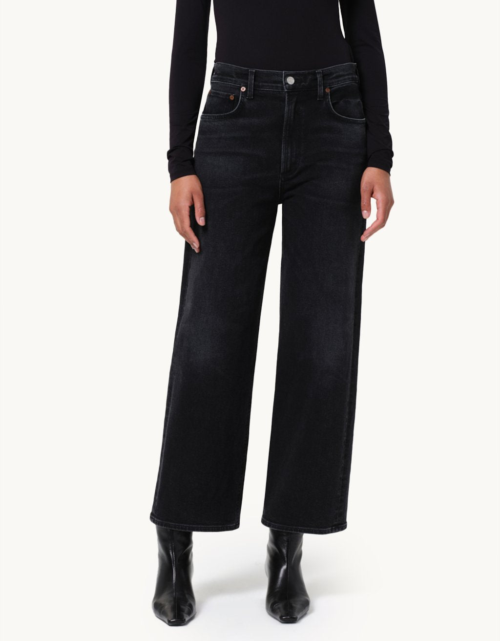 Person wearing black wide-leg jeans with a black top and booties on a neutral background