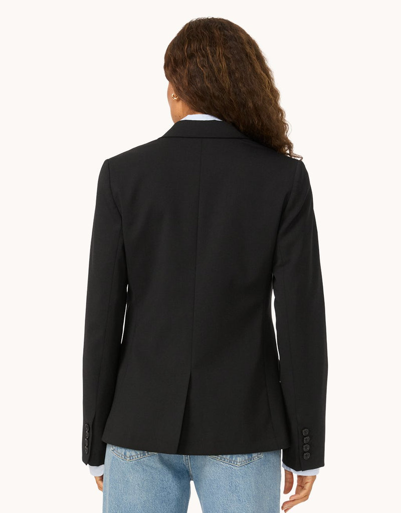 Back view of a woman wearing a black blazer on a light gray background