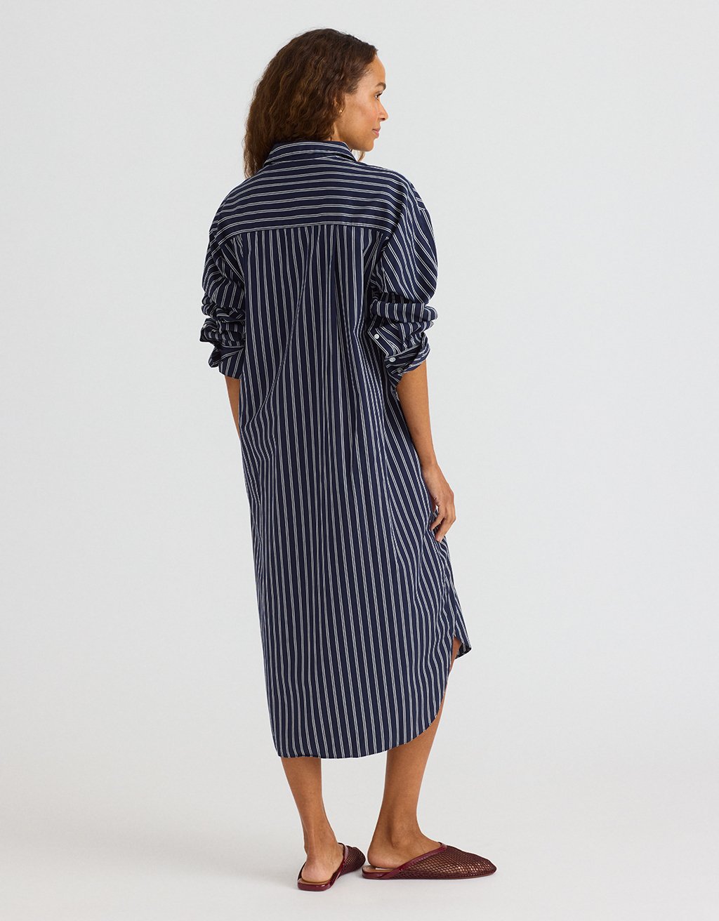 Woman wearing a navy and white striped shirtdress on a light gray background